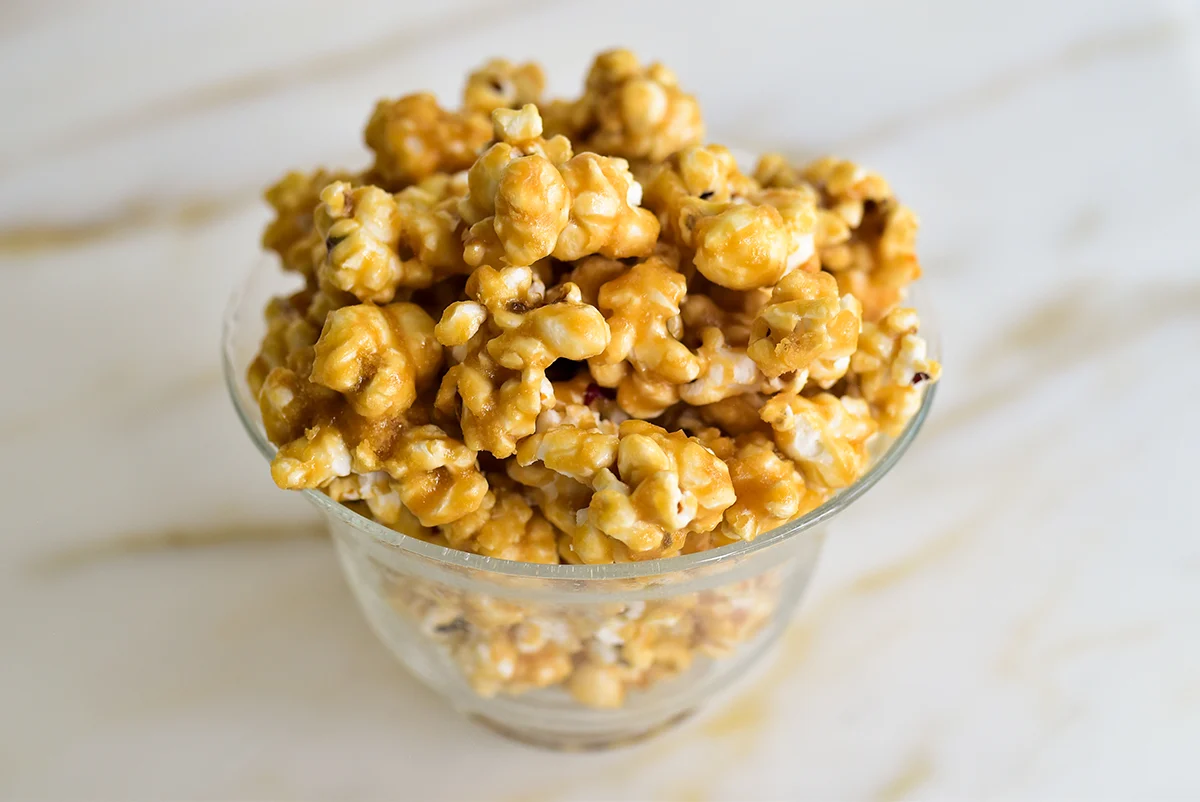 A large bowl of sweet and salty popcorn mix with chocolate chunks and pretzels on a cozy kitchen counter under warm lighting