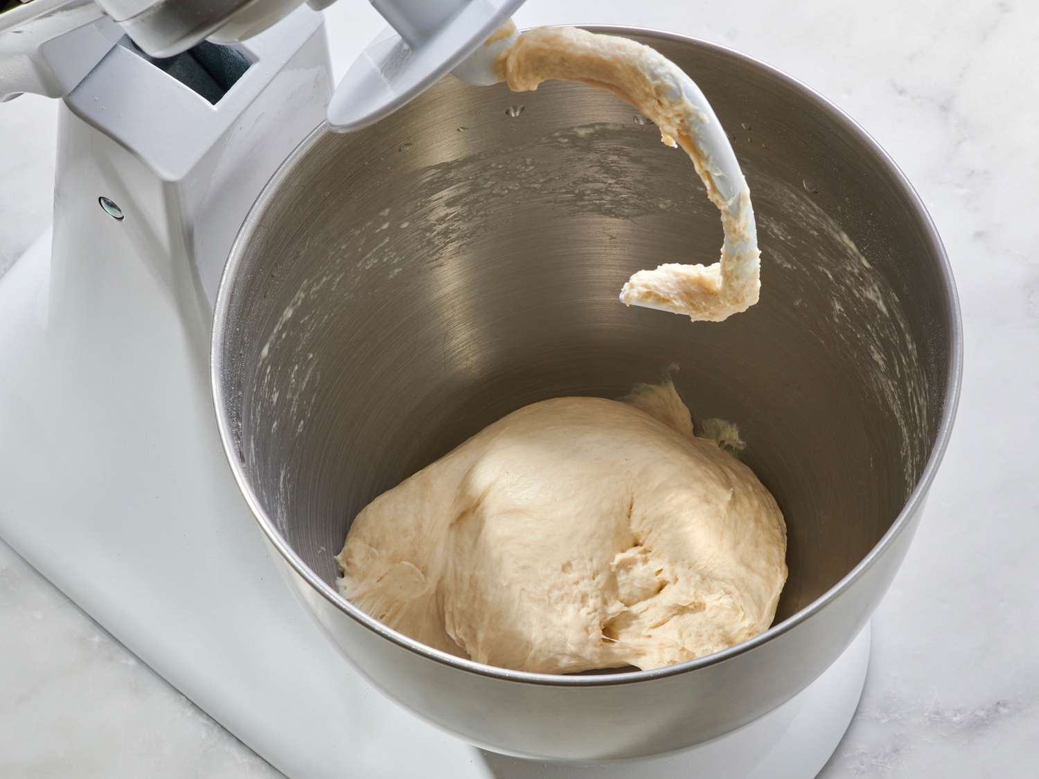 A large bowl with flour, yeast, salt, and warm water being stirred into a shaggy pizza dough on a clean kitchen counter