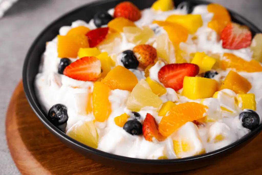 A large glass bowl filled with creamy Cool Whip fruit salad with mandarin oranges, pineapple, and mini marshmallows on a bright kitchen counter
