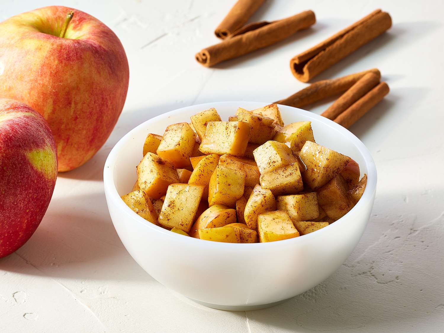 A large glass bowl filled with peeled sliced apples tossed with cinnamon, sugar, and lemon juice on a kitchen counter