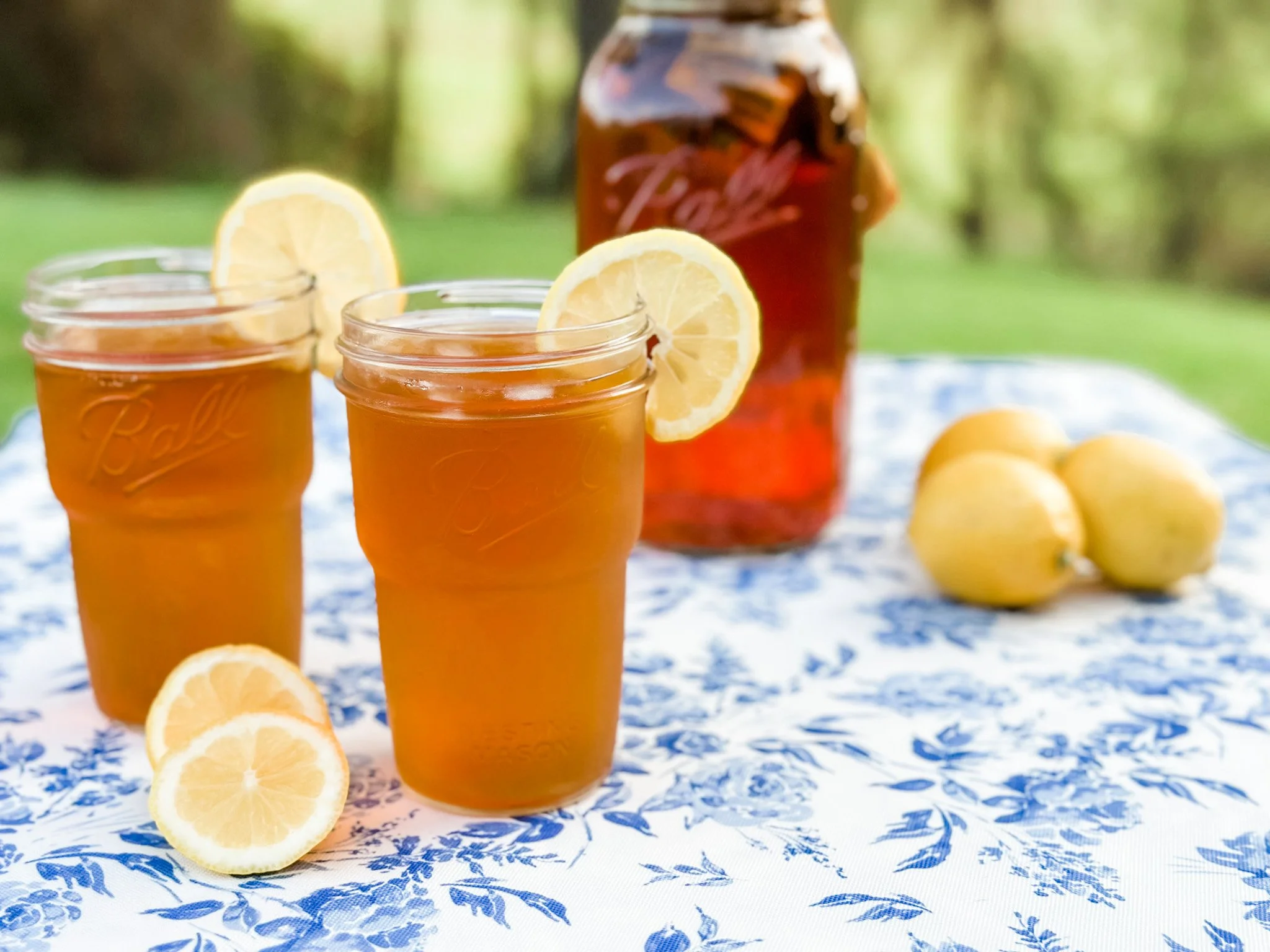 A large glass jar of sun tea on a sunny kitchen counter with lemon slices floating inside and condensation on the glass