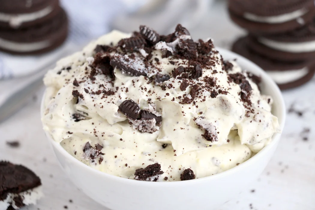 A large glass mixing bowl filled with Oreo fluff as crushed cookies are folded into the creamy mixture