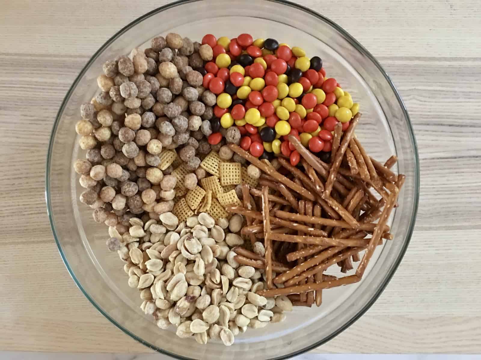 A large mixing bowl filled with Chex cereal, mini pretzels, and peanuts ready to be coated on a kitchen counter