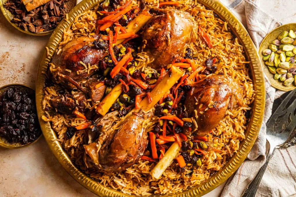 A large platter of Kabuli pulao with fluffy basmati rice, tender lamb pieces, caramelized carrot strips, and golden raisins, set on a warm-toned dinner table
