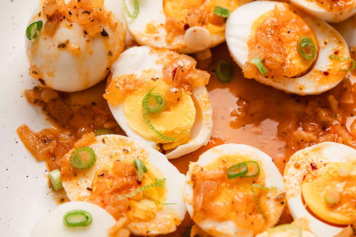 A large platter piled with shrimp, sausage slices, corn rounds, baby potatoes, and halved boiled eggs coated in a glossy buttery Cajun-style sauce on a rustic kitchen table