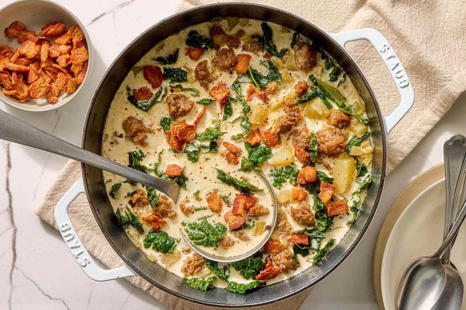 A large pot of Zuppa Toscana soup simmering on a stovetop with visible potato slices and sausage crumbles before the cream is added