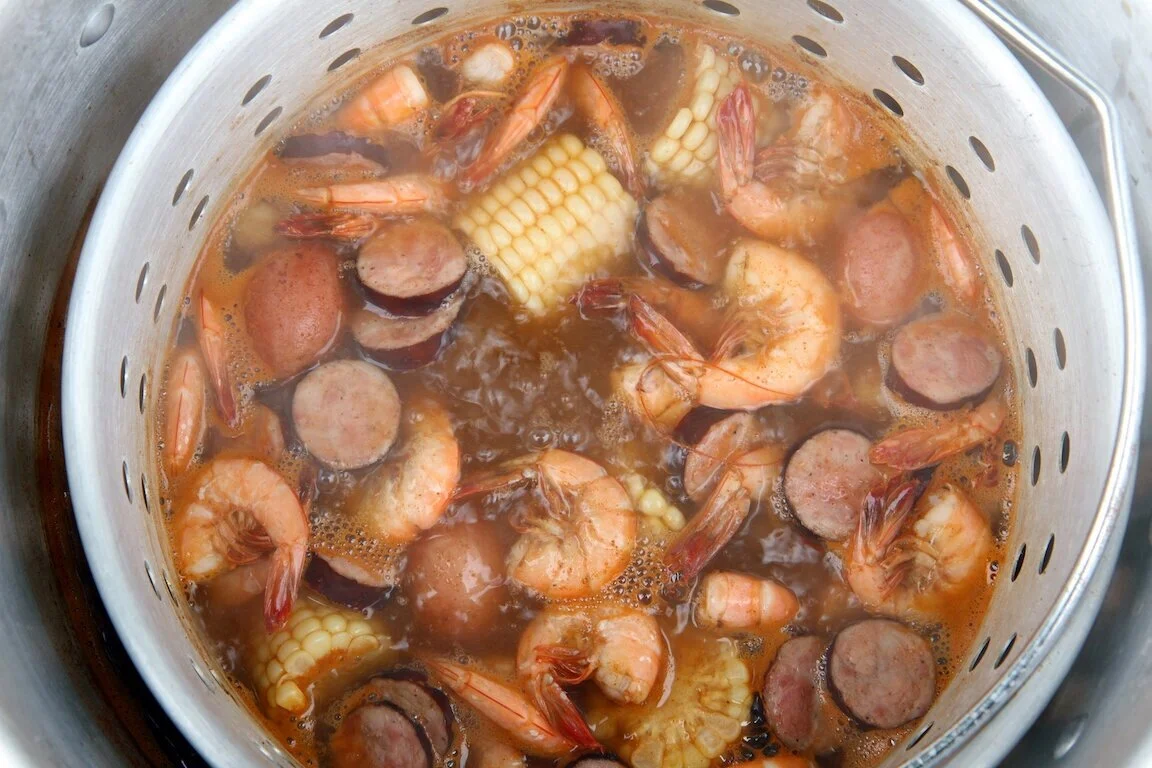 A large pot of boiling seasoned water with lemon halves, onion pieces, and garlic floating at the surface