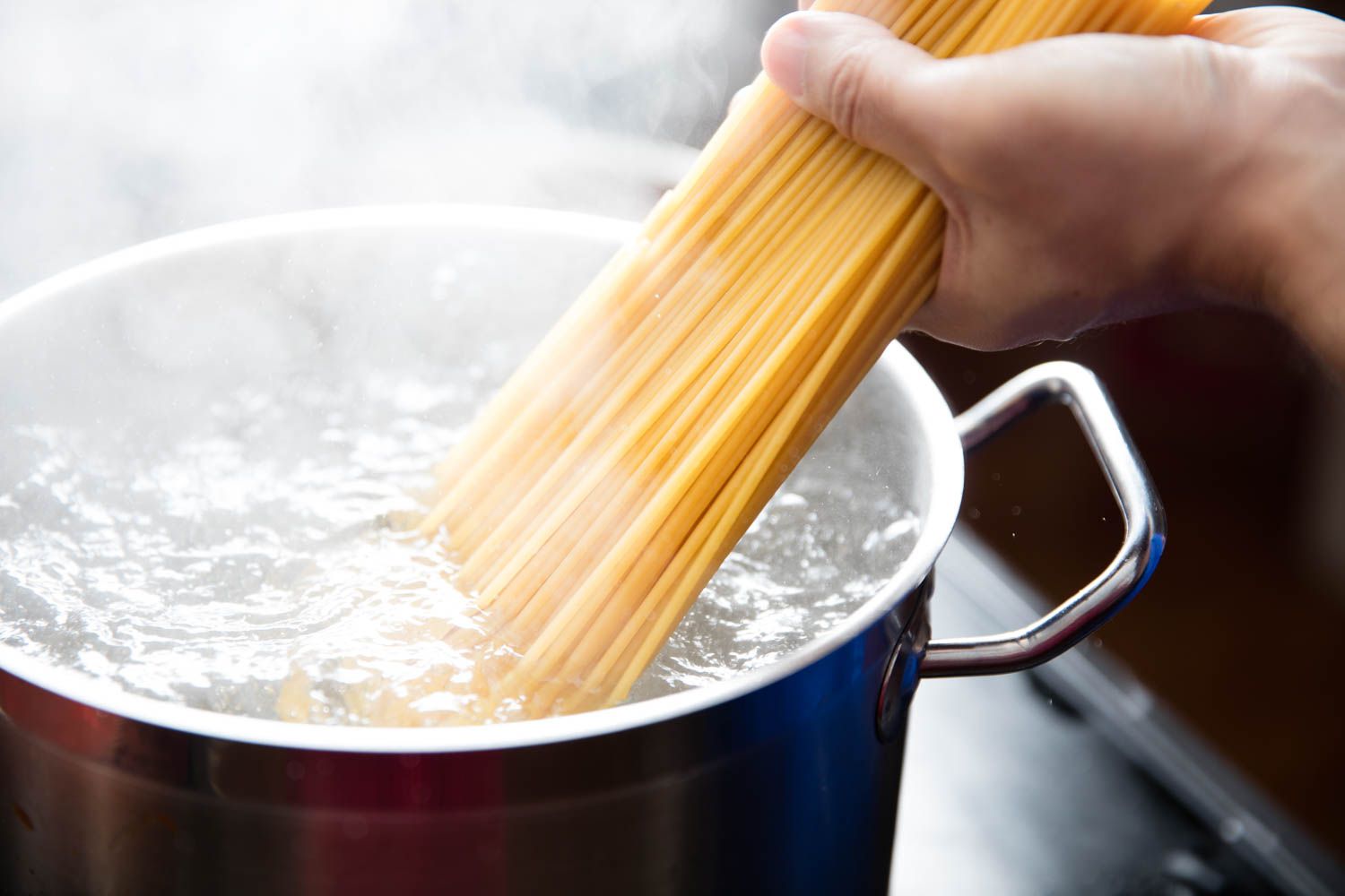 A large pot of pasta boiling on a stovetop with steam rising in a bright home kitchen