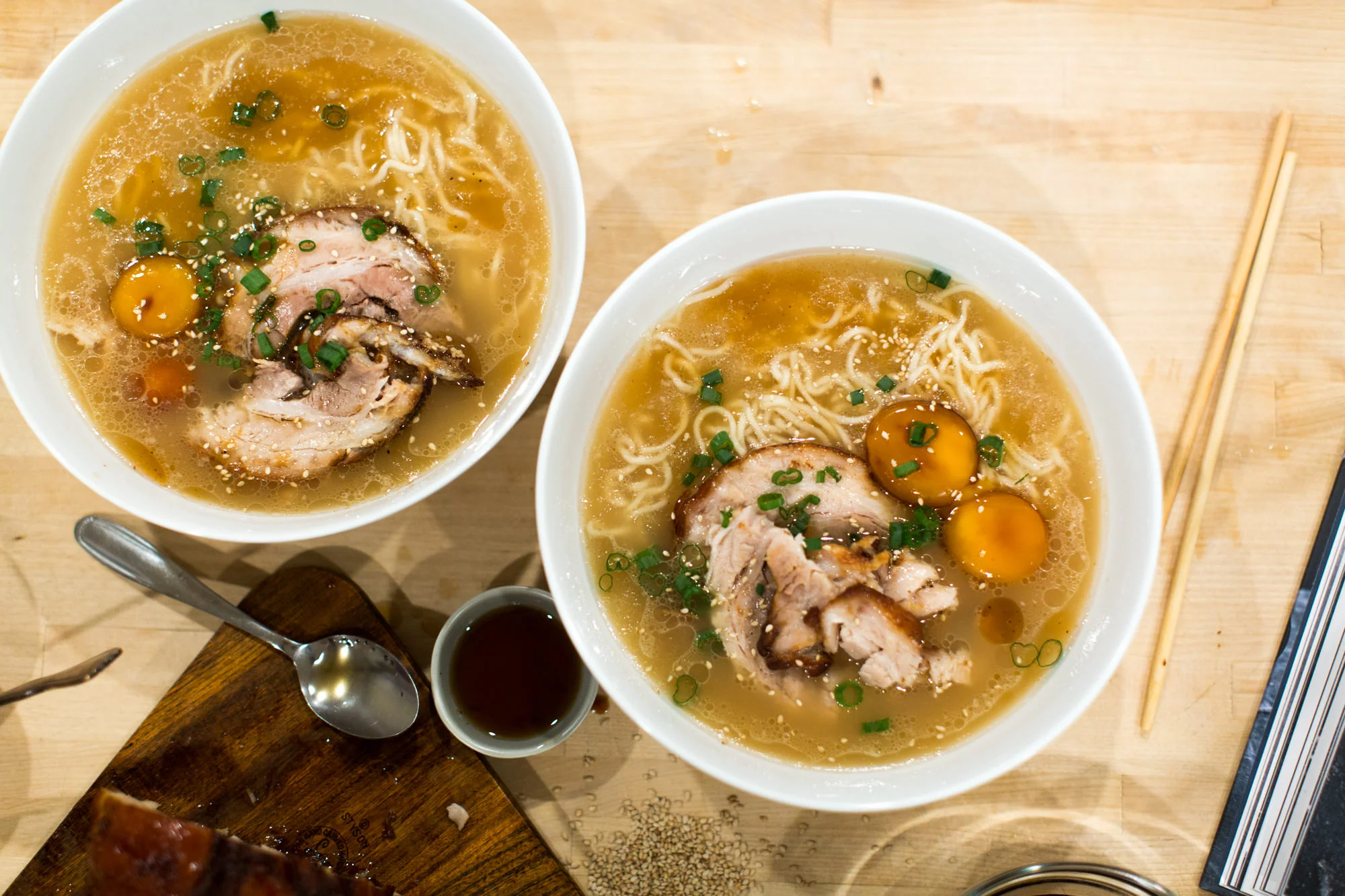 A large pot of steaming homemade ramen broth on a stovetop with a ladle resting on the rim, warm kitchen lighting