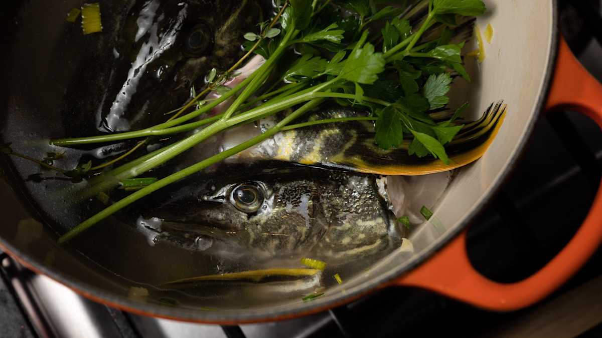 A large pot on a stovetop with tomato fish soup gently simmering, visible fennel slices and herbs in the broth