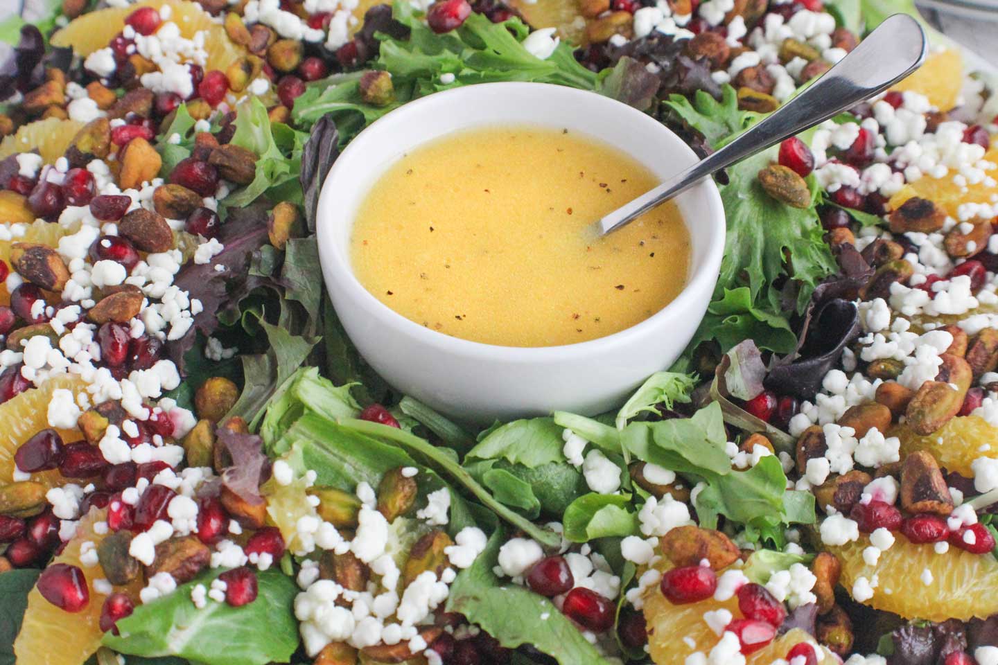 A large serving bowl of Christmas salad with mixed greens, sliced pears, dried cranberries, candied pecans, and crumbled feta, lightly dressed and set on a warm kitchen table with soft holiday lighting