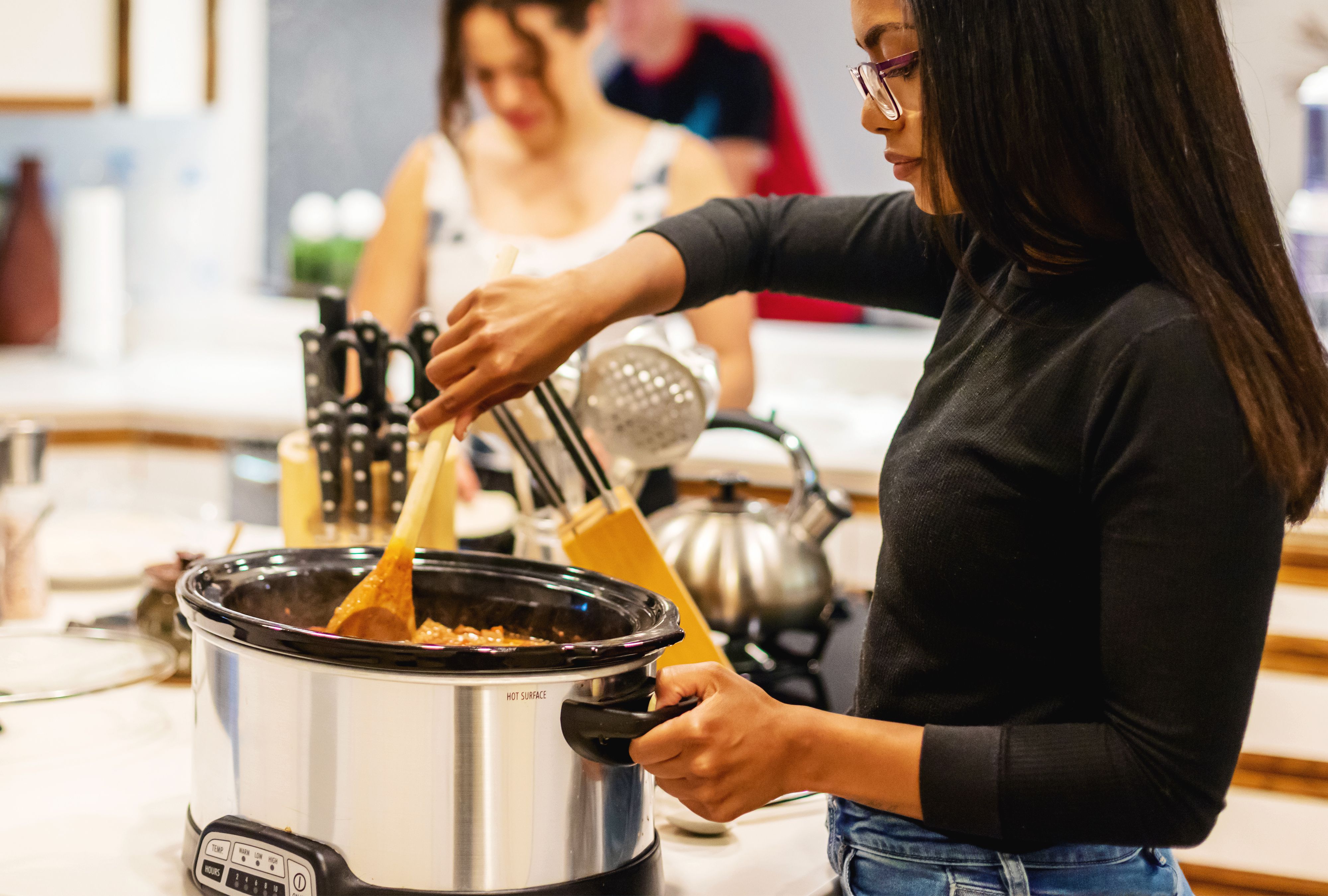 A large slow cooker sitting on a tidy kitchen counter next to a cutting board and tongs