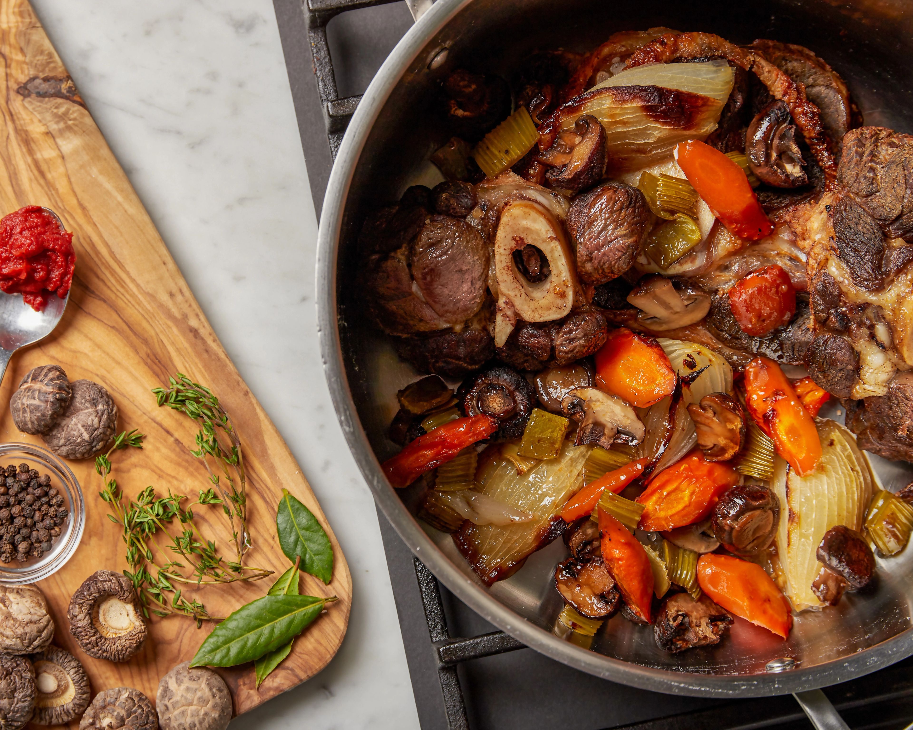 A large stockpot of clear amber beef broth gently simmering on a stovetop with roasted beef bones and vegetables nearby on a warm kitchen counter