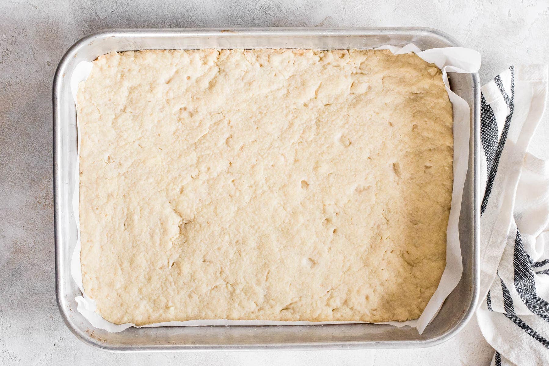 A lightly golden baked shortbread crust in a parchment-lined square baking pan resting on a cooling rack