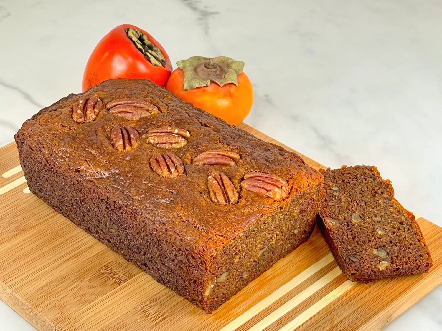 A loaf of persimmon bread wrapped in parchment and plastic wrap on a kitchen counter next to an airtight container