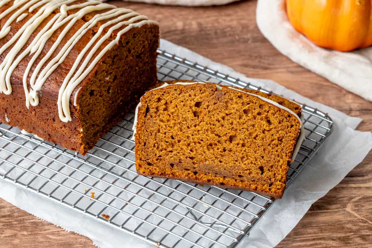 A loaf of pumpkin bread cooling on a wire rack with parchment paper underneath