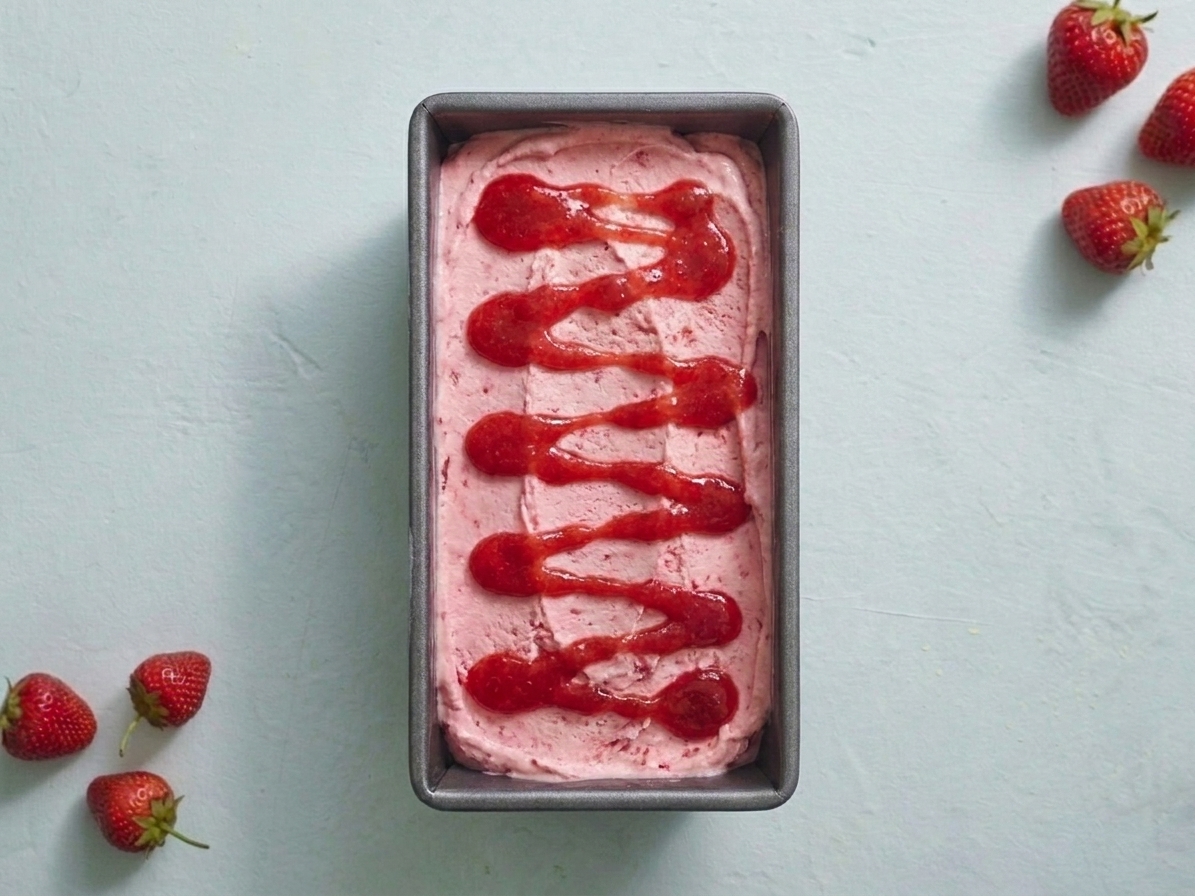 A loaf pan of no-churn strawberry ice cream with visible strawberry swirl patterns on top, sitting on a kitchen counter