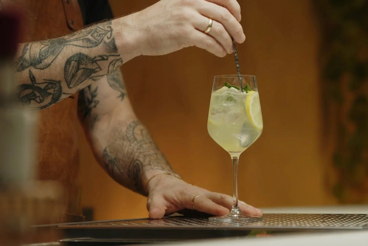 A long spoon gently stirring a pale yellow limoncello spritz in a stemmed glass with ice