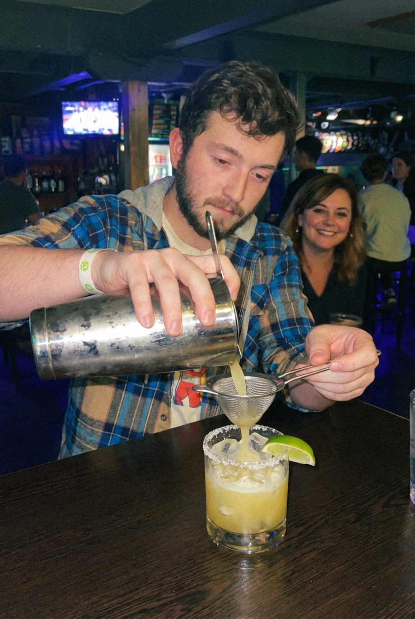 A margarita being strained from a cocktail shaker into a salted rocks glass filled with ice