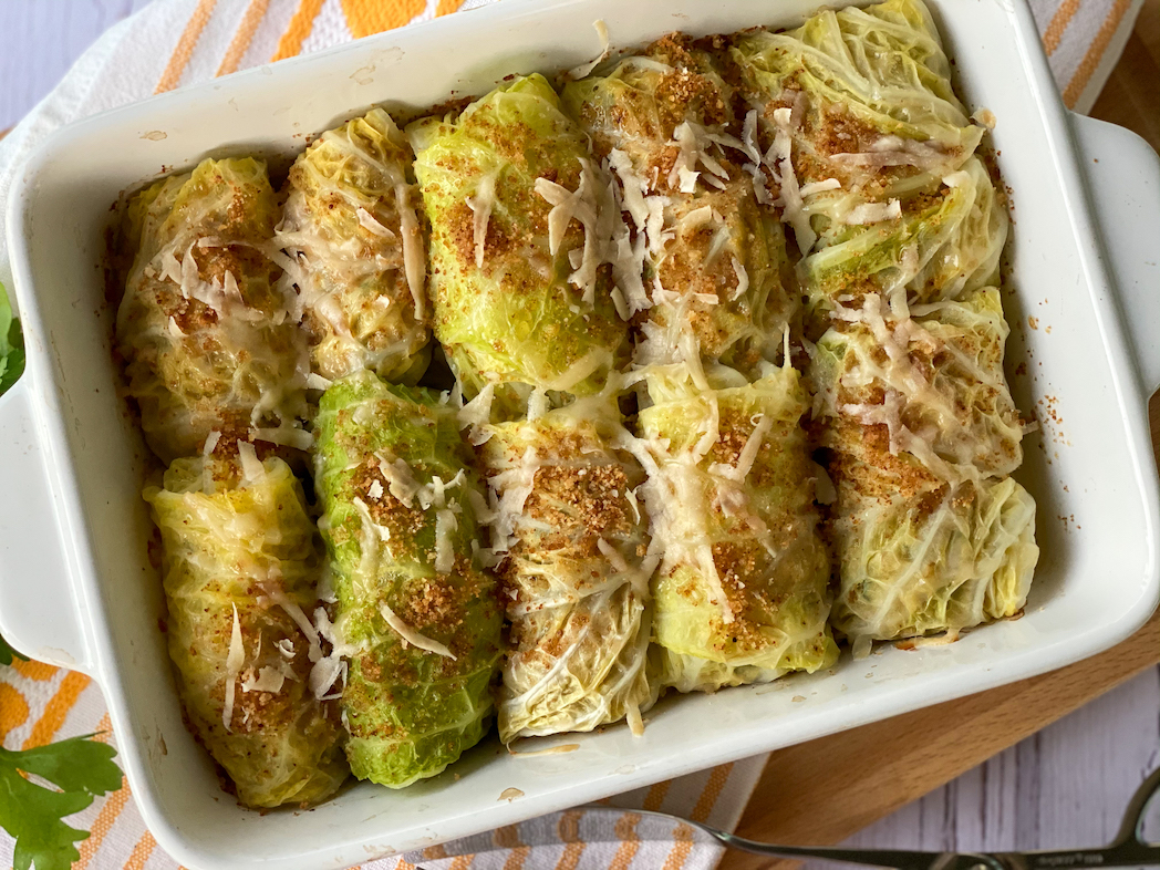 A meal prep container holding leftover cabbage rolls covered in tomato sauce with a lid set beside it on a kitchen counter
