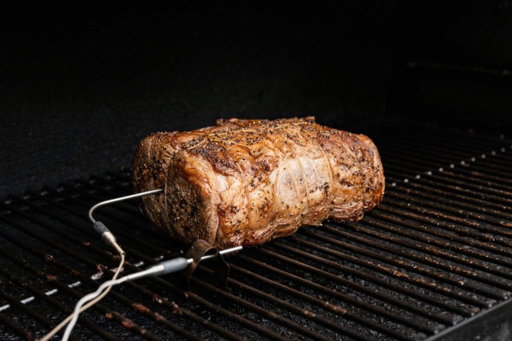 A meat thermometer inserted into the thickest center of a boneless rib roast sitting in a roasting pan on a home kitchen counter under warm lighting