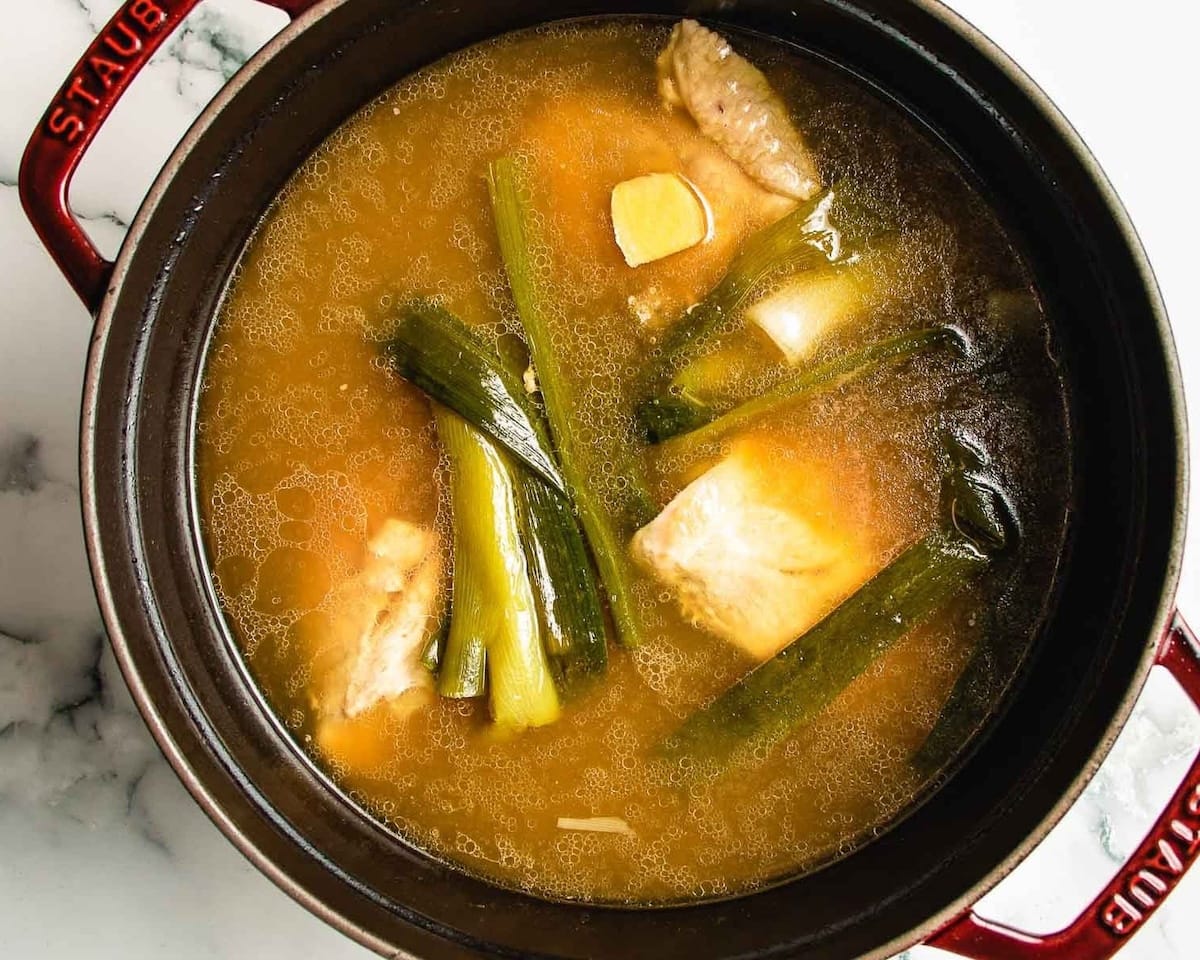 A medium saucepan of broth at a gentle simmer with grated ginger dispersed in the liquid on a home stove