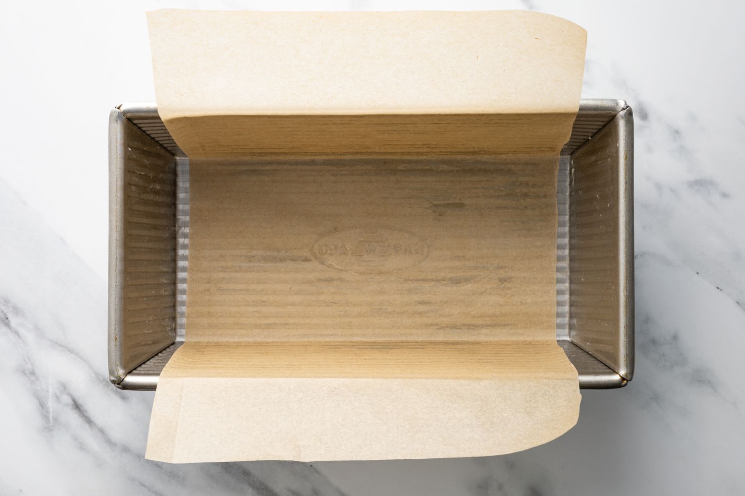 A metal 9x5-inch loaf pan lined with parchment paper on a kitchen counter, ready for cake batter