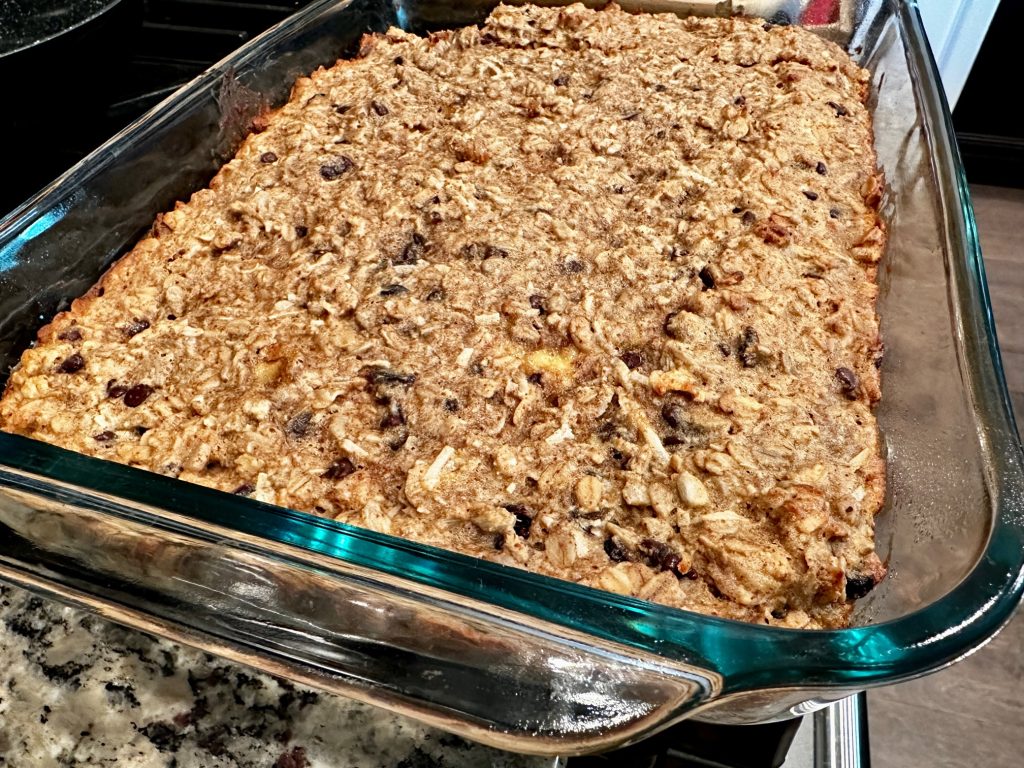 A metal baking pan filled with golden-brown cinnamon oatmeal bars, cut into neat rectangles on a light kitchen counter with soft natural window light