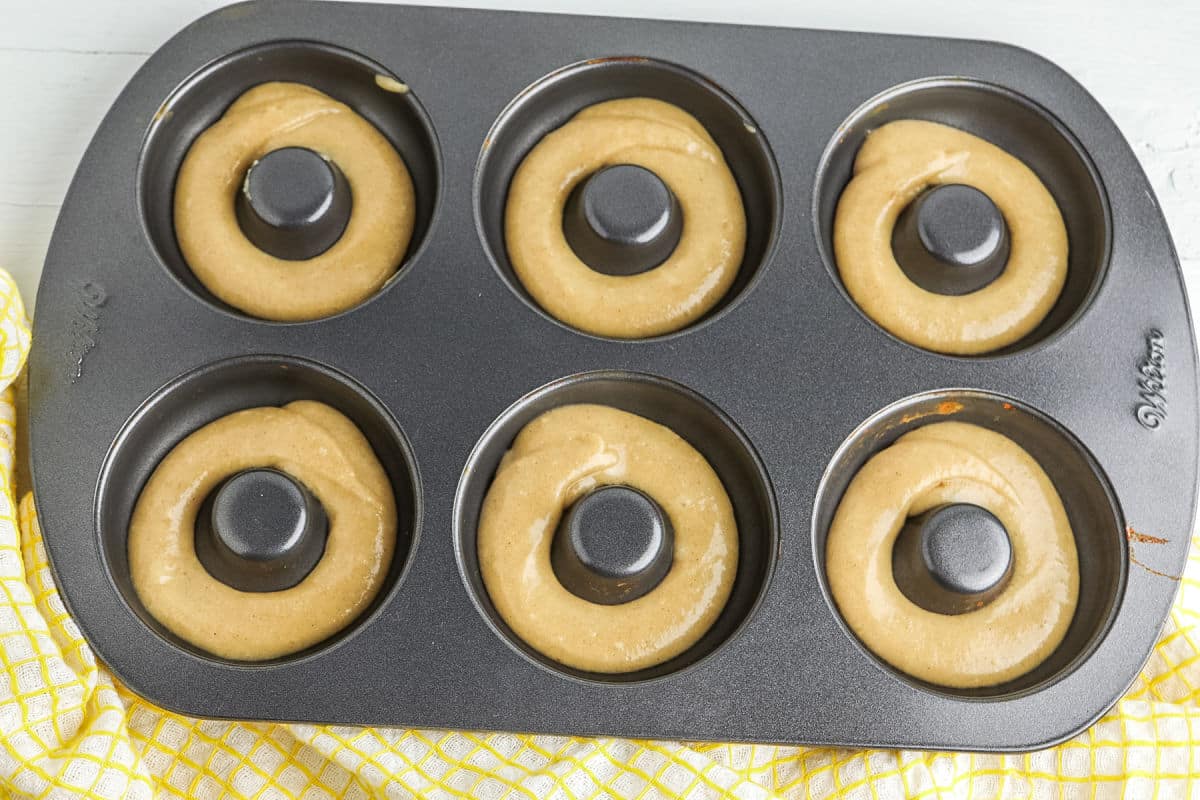 A metal donut pan on a kitchen counter being lightly greased with butter or nonstick spray