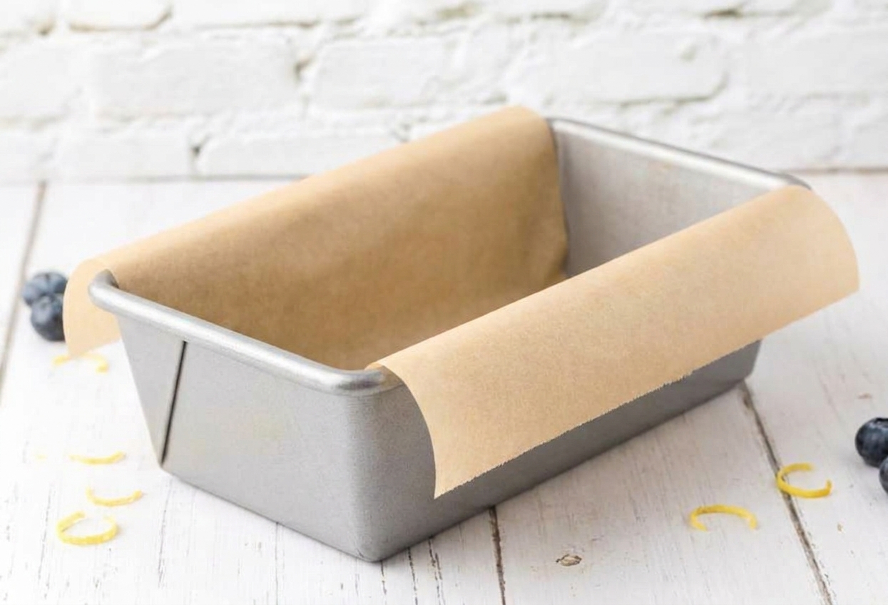 A metal loaf pan lined with parchment paper with overhang on both sides, sitting on a clean kitchen counter