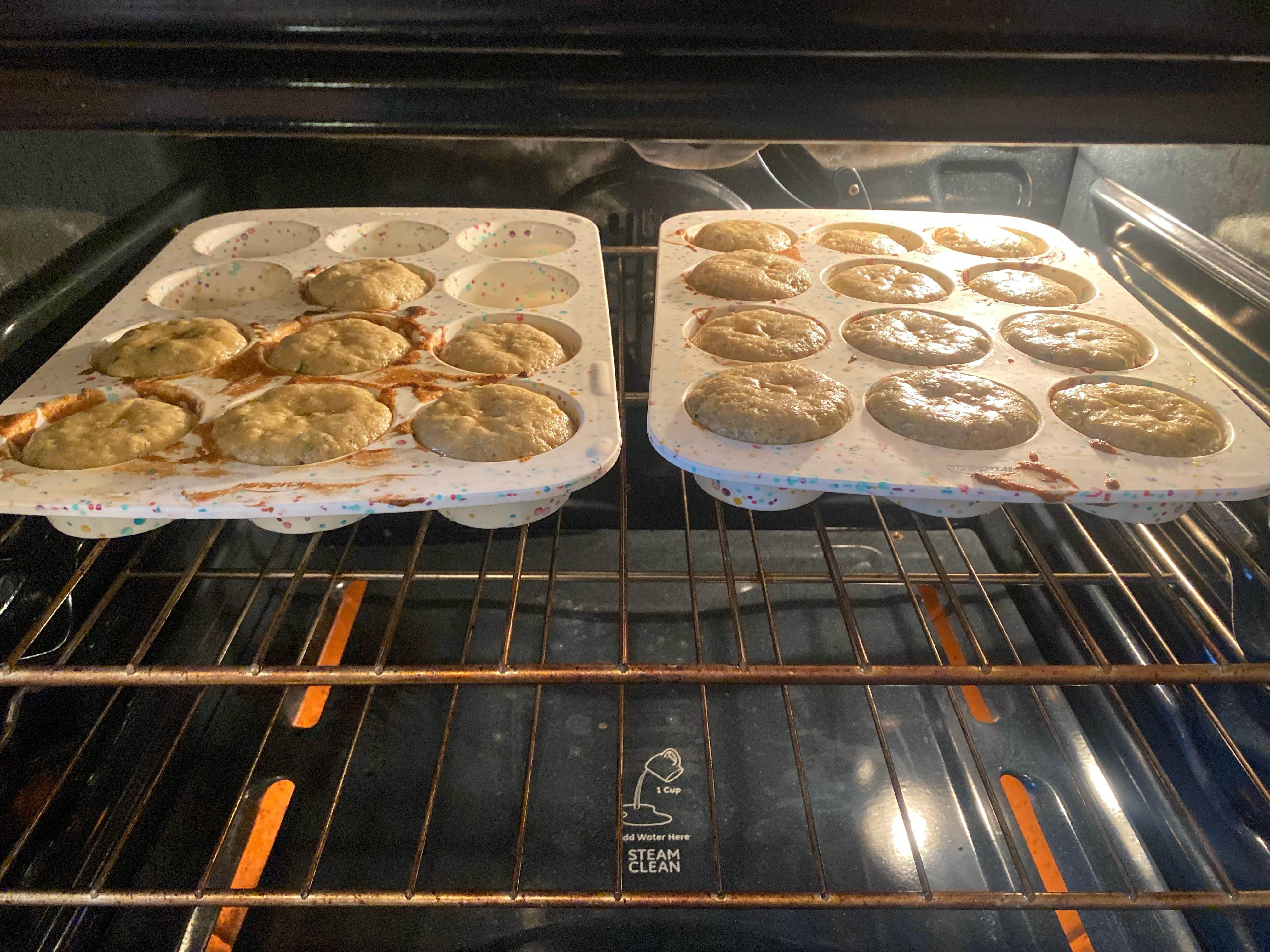 A metal muffin tin heating on the middle rack of an oven with the oven light on