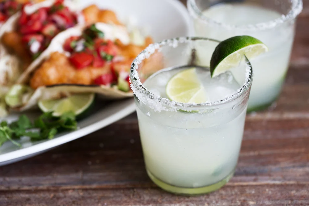 A mezcal margarita in a rocks glass with a salted rim and a lime wheel, sitting on a warm-toned kitchen counter with soft natural light