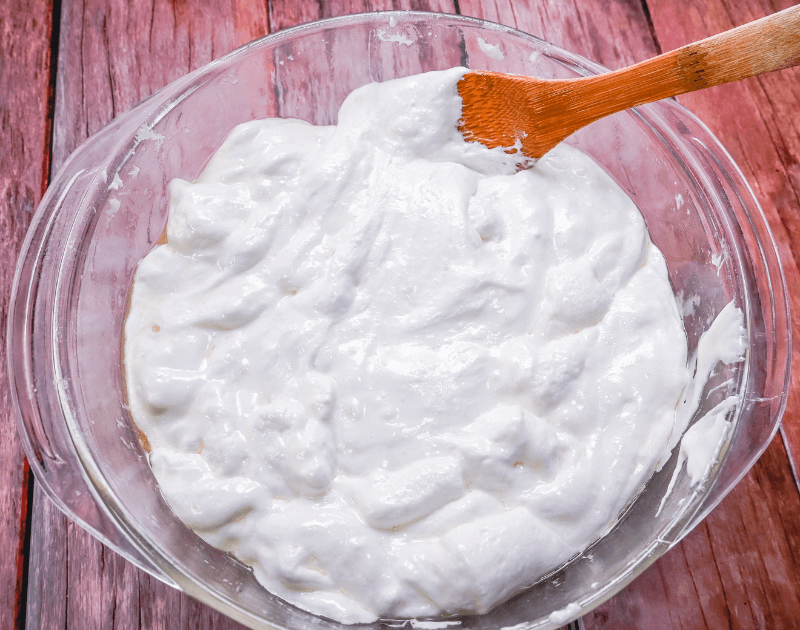 A microwave-safe bowl of melted marshmallows being stirred with a silicone spatula on a kitchen counter