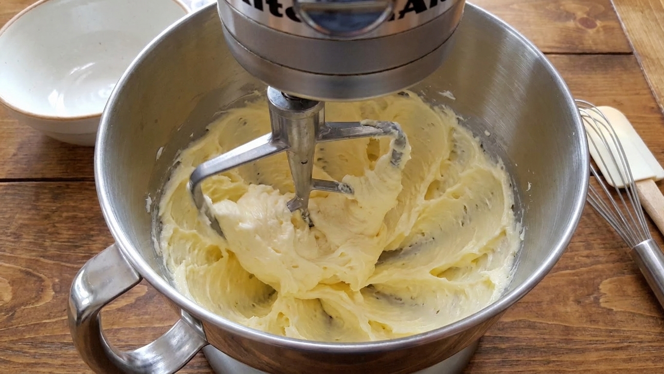 A mixer beating softened butter in a stainless steel bowl as it turns pale and fluffy