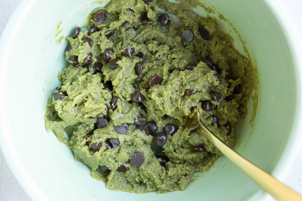 A mixing bowl filled with bright green cookie dough with a spatula resting inside on a kitchen counter