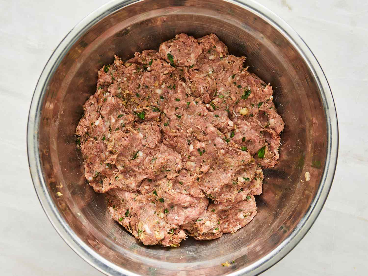 A mixing bowl filled with ground beef kafta mixture speckled with parsley and spices on a kitchen counter
