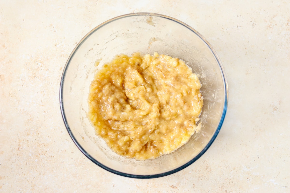 A mixing bowl filled with mashed ripe bananas on a kitchen counter with a fork resting inside