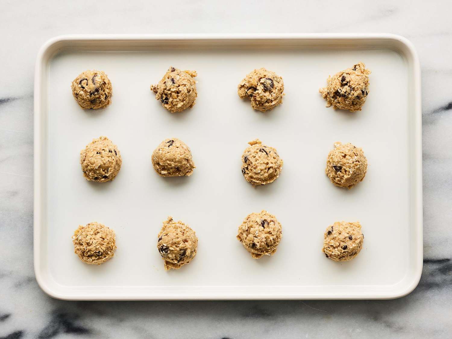 A mixing bowl of oatmeal cookie dough with visible rolled oats being stirred with a rubber spatula on a kitchen counter