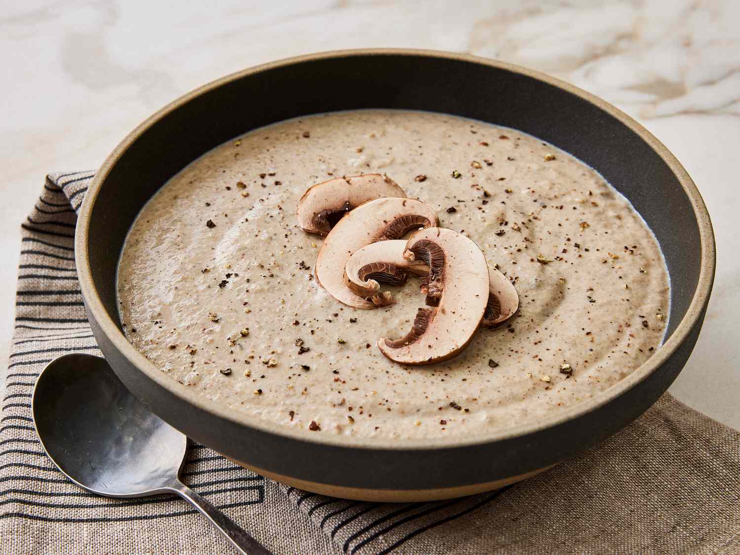 A mixing bowl on a kitchen counter with cream of mushroom soup, milk, soy sauce, and black pepper being stirred together with a spatula