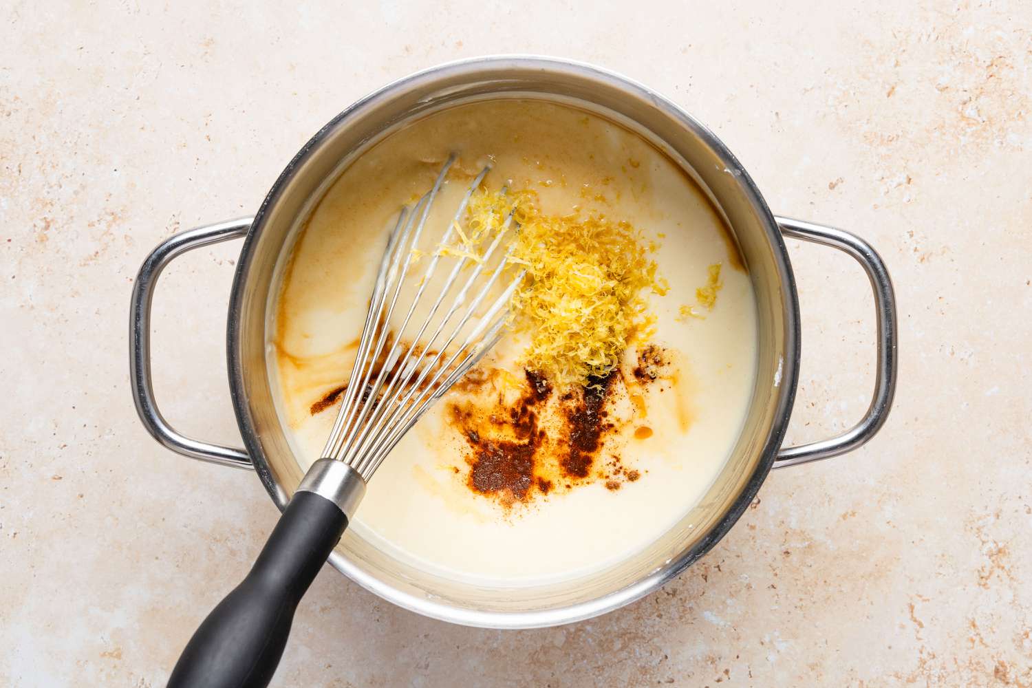 A mixing bowl with drained ricotta, semolina, sugar, and fresh orange zest ready to be stirred together on a kitchen counter