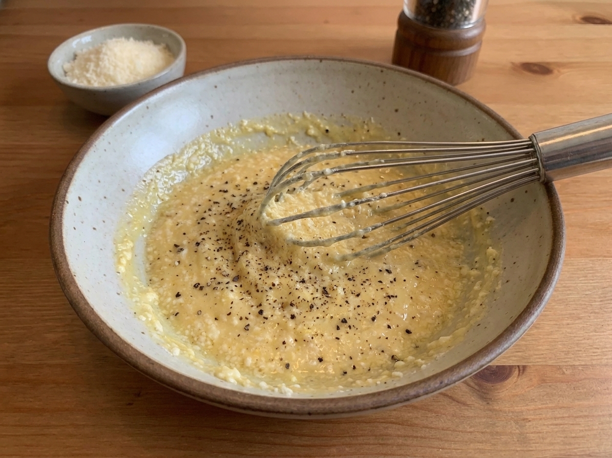 A mixing bowl with egg yolks, whole eggs, grated Pecorino Romano, and black pepper whisked into a thick, pale yellow paste