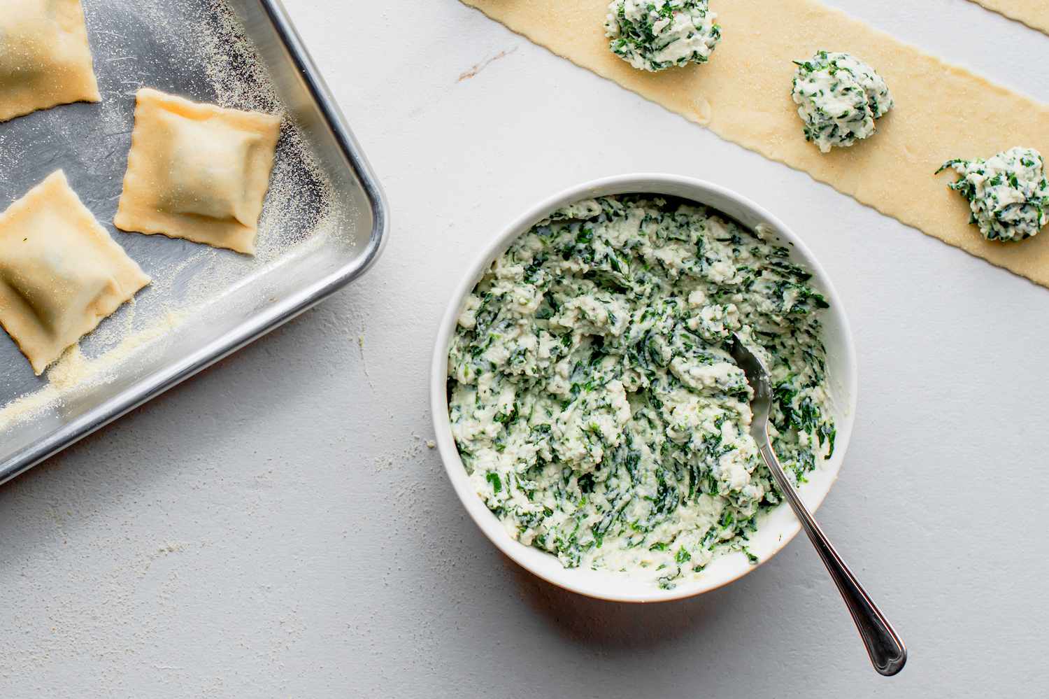 A mixing bowl with ricotta, Parmesan, chopped spinach, garlic, and herbs being stirred together on a kitchen counter