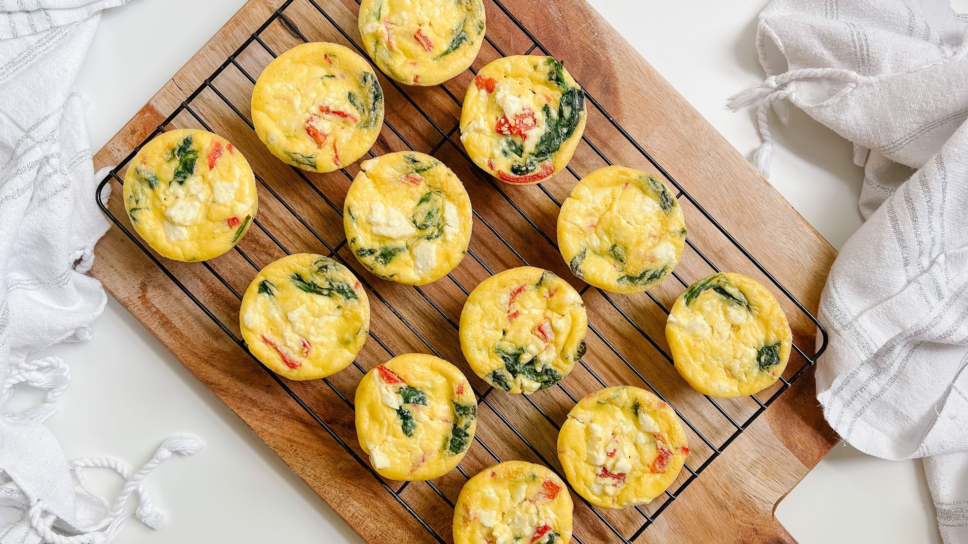 A muffin tin, eggs, cottage cheese, shredded cheddar, spinach, and diced bell pepper arranged on a bright kitchen counter