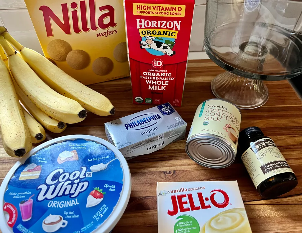 A neat lineup of ingredients for banana pudding including bananas, vanilla wafers, milk, sugar, eggs, cornstarch, butter, vanilla, and salt arranged on a kitchen counter