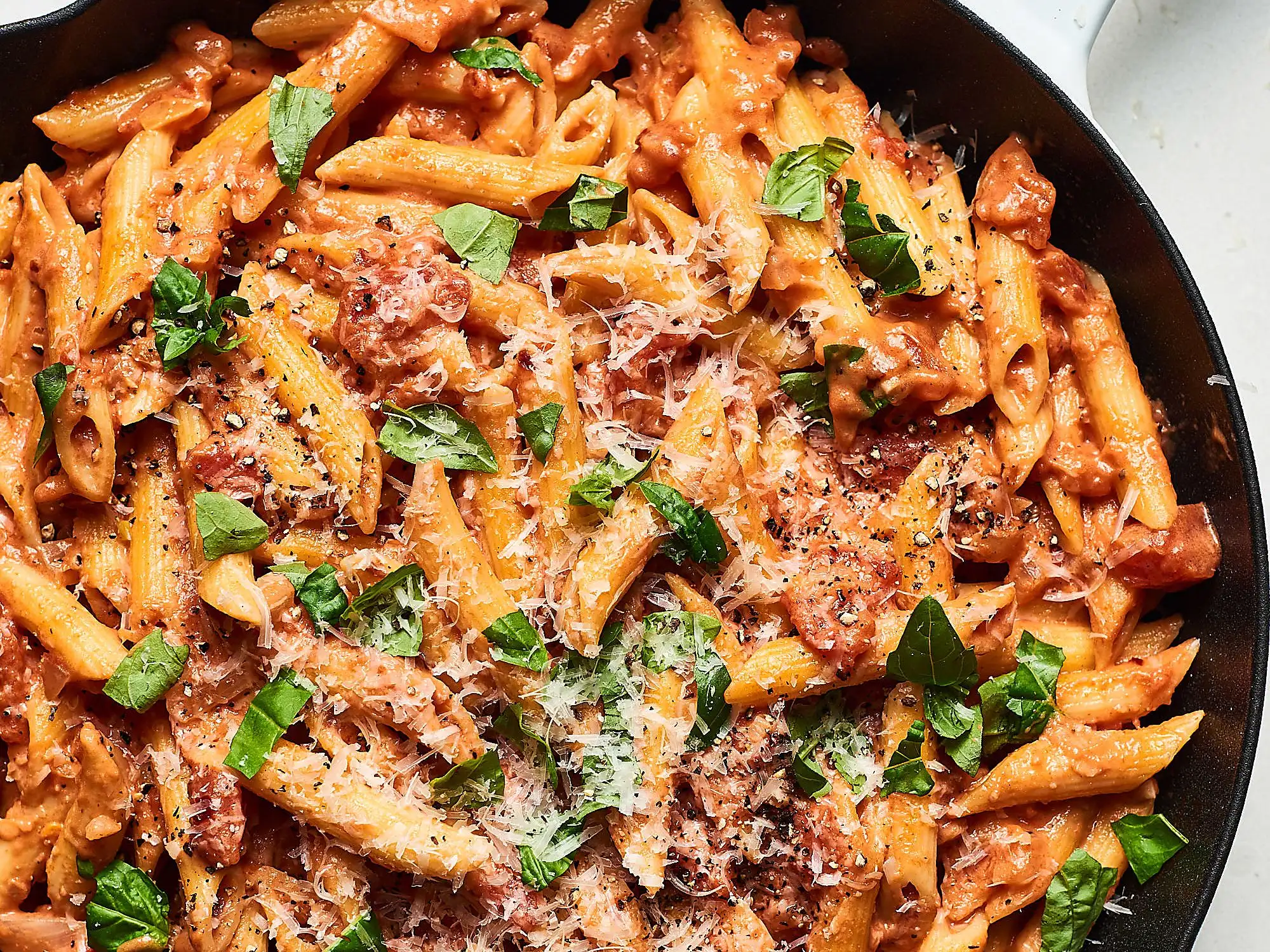 A neat lineup of ingredients on a kitchen counter including garlic, onion, canned tomatoes, pasta, cream, Parmesan, and basil