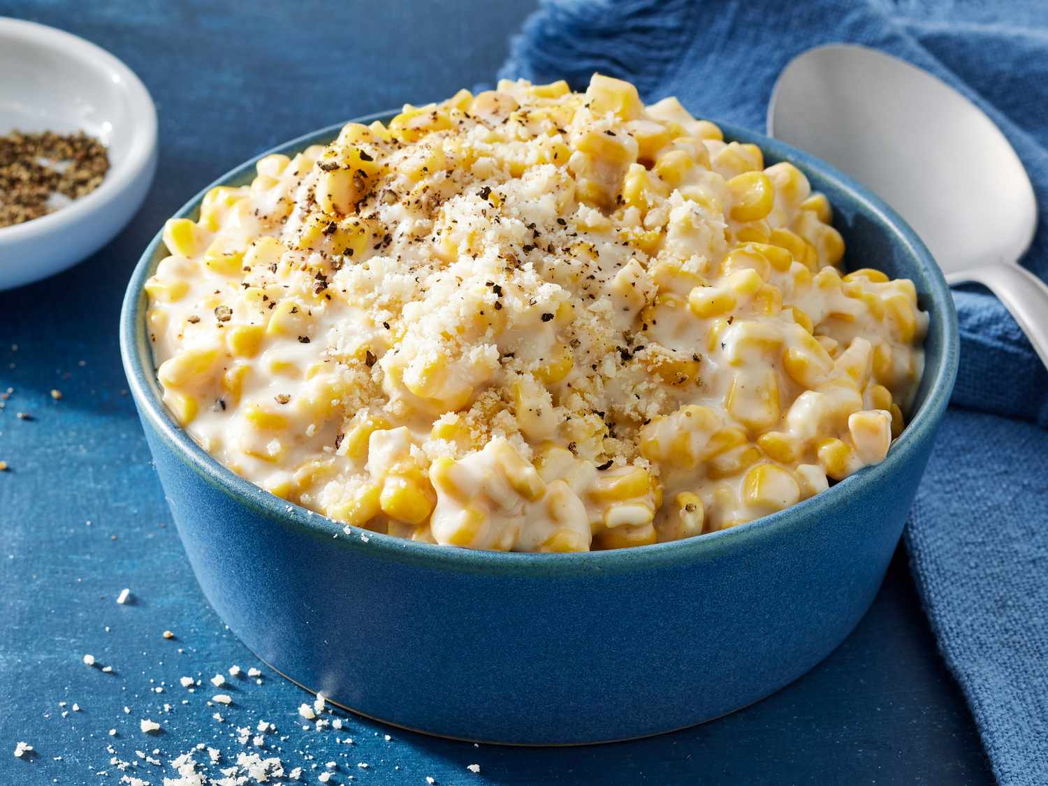 A neat lineup of ingredients on a light kitchen counter: a bowl of corn kernels, butter, milk, cream, flour, sugar, salt, black pepper, and a small dish of minced garlic