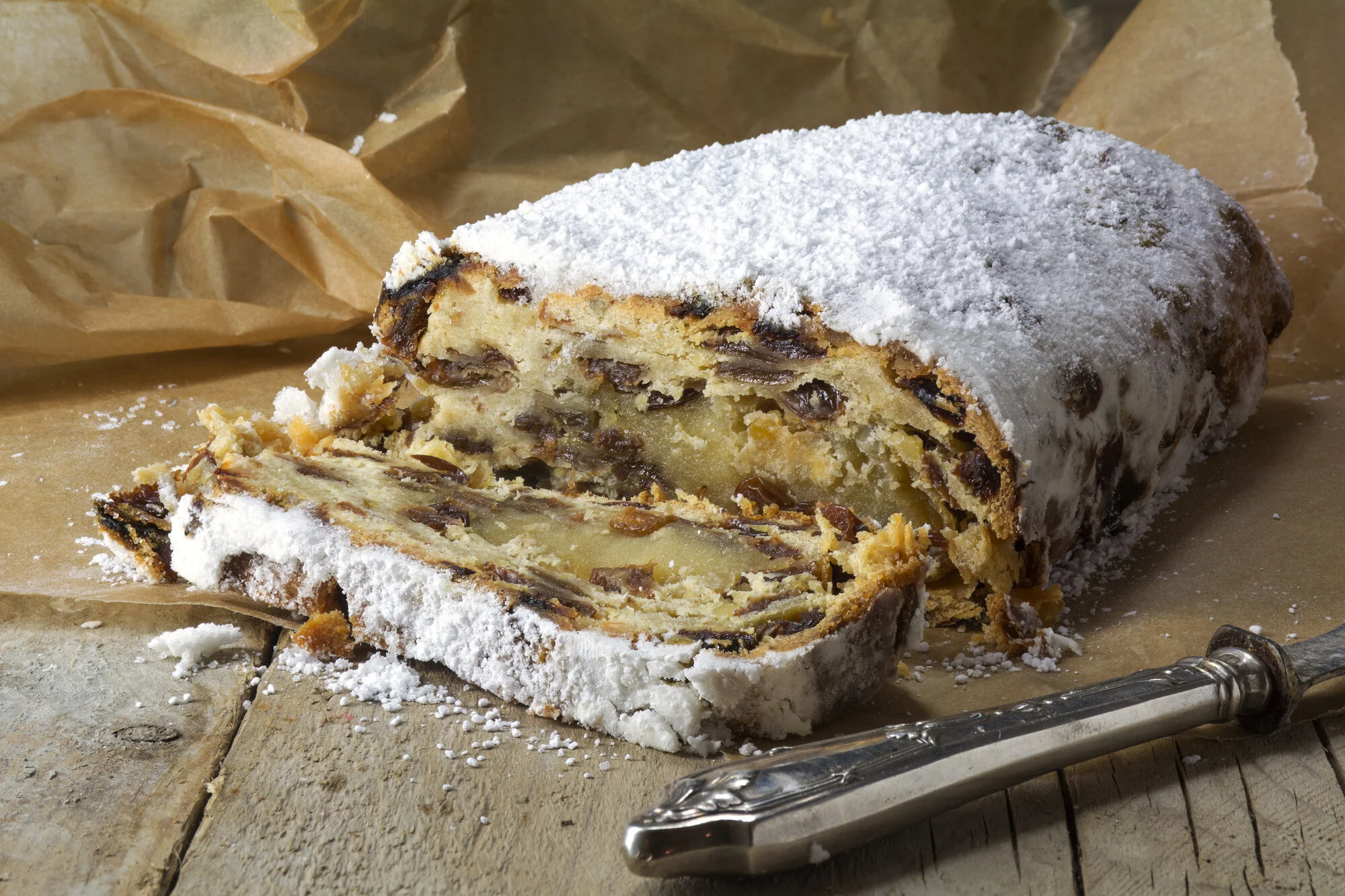 A neat log of homemade marzipan on parchment paper with a small bowl of powdered sugar and whole almonds on a warm kitchen counter