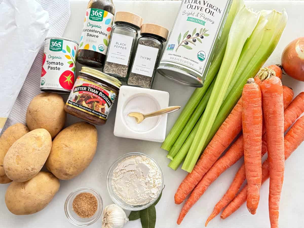 A neat spread of stew ingredients on a home kitchen counter including beef chuck, potatoes, carrots, onion, garlic, dried guajillo chiles, canned tomatoes, and spices