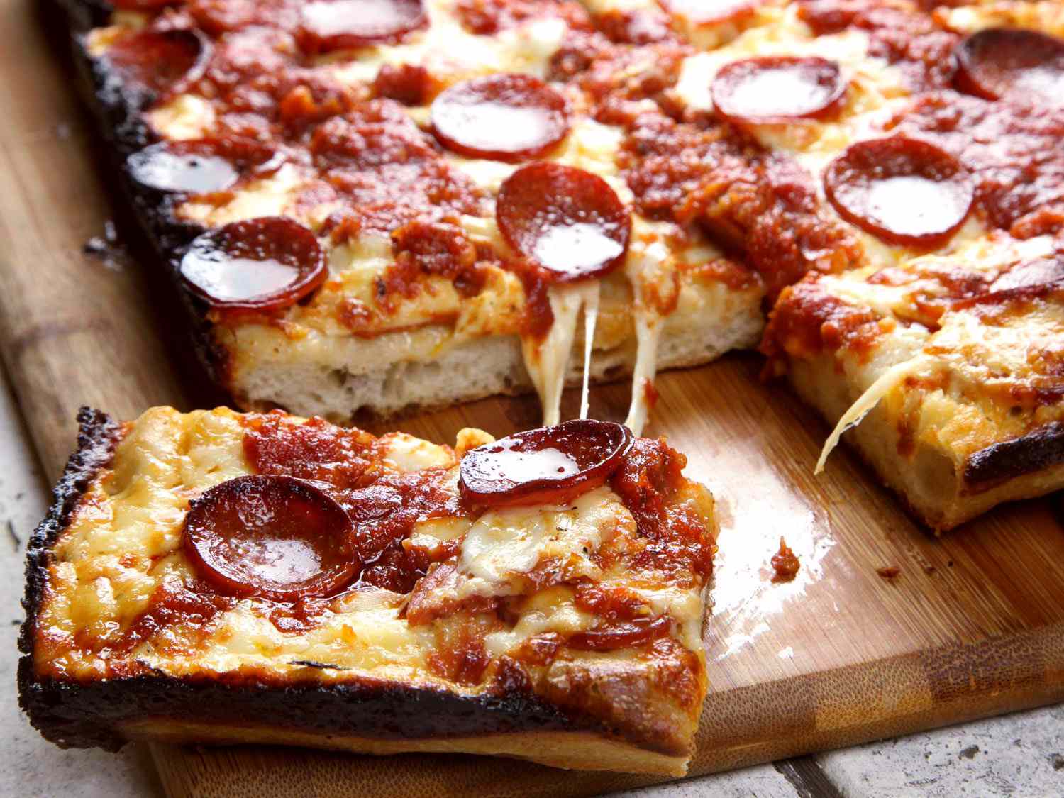 A neatly arranged set-of deep pan pizza ingredients on a kitchen counter including flour, yeast, olive oil, canned tomatoes, mozzarella, pepperoni, and a cast iron skillet