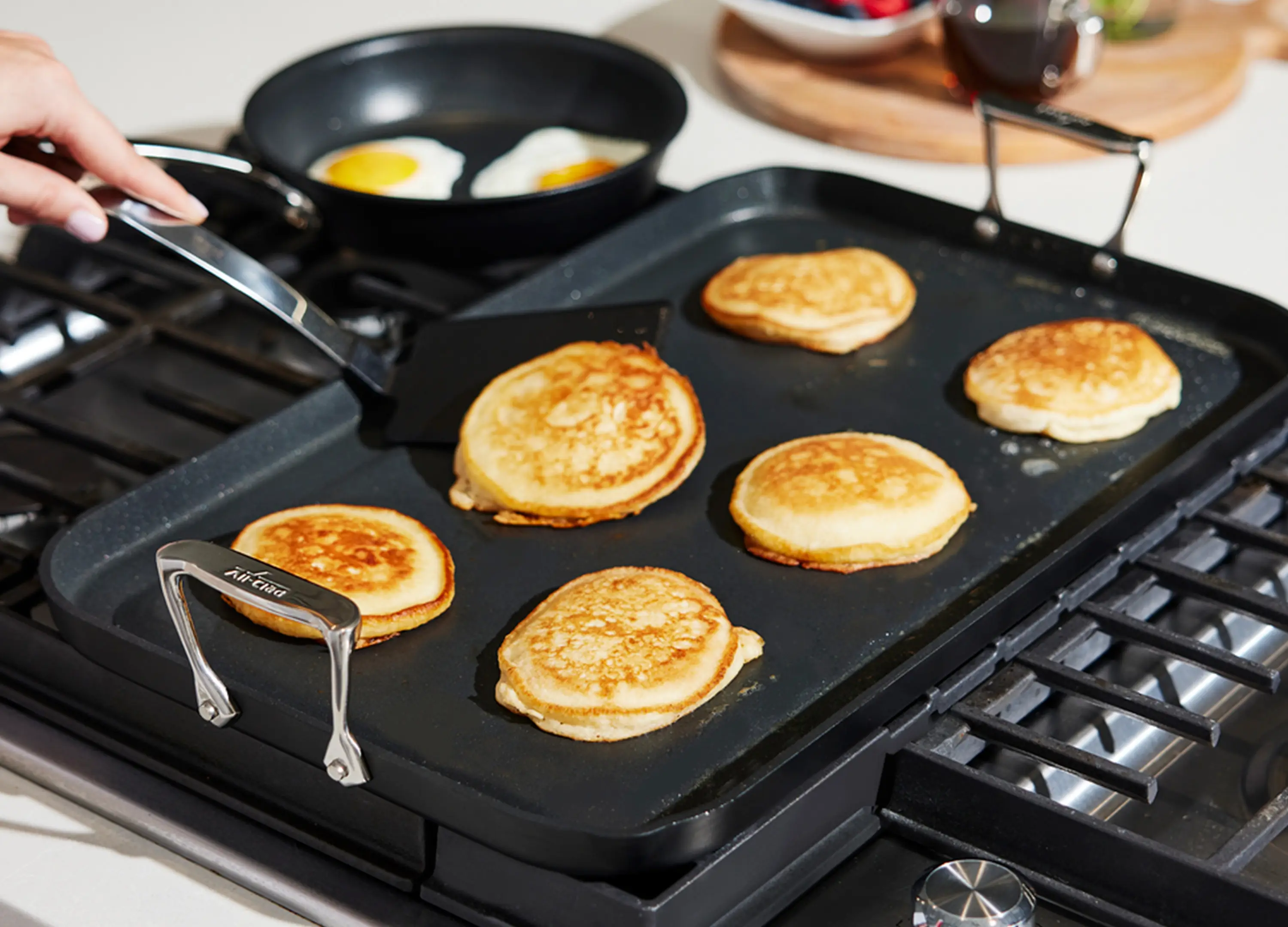 A nonstick skillet on a home stovetop with small rounds of keto pancake batter cooking and a spatula resting nearby